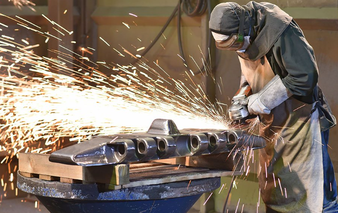 Grinding a metal part with sparks; operator in PPE